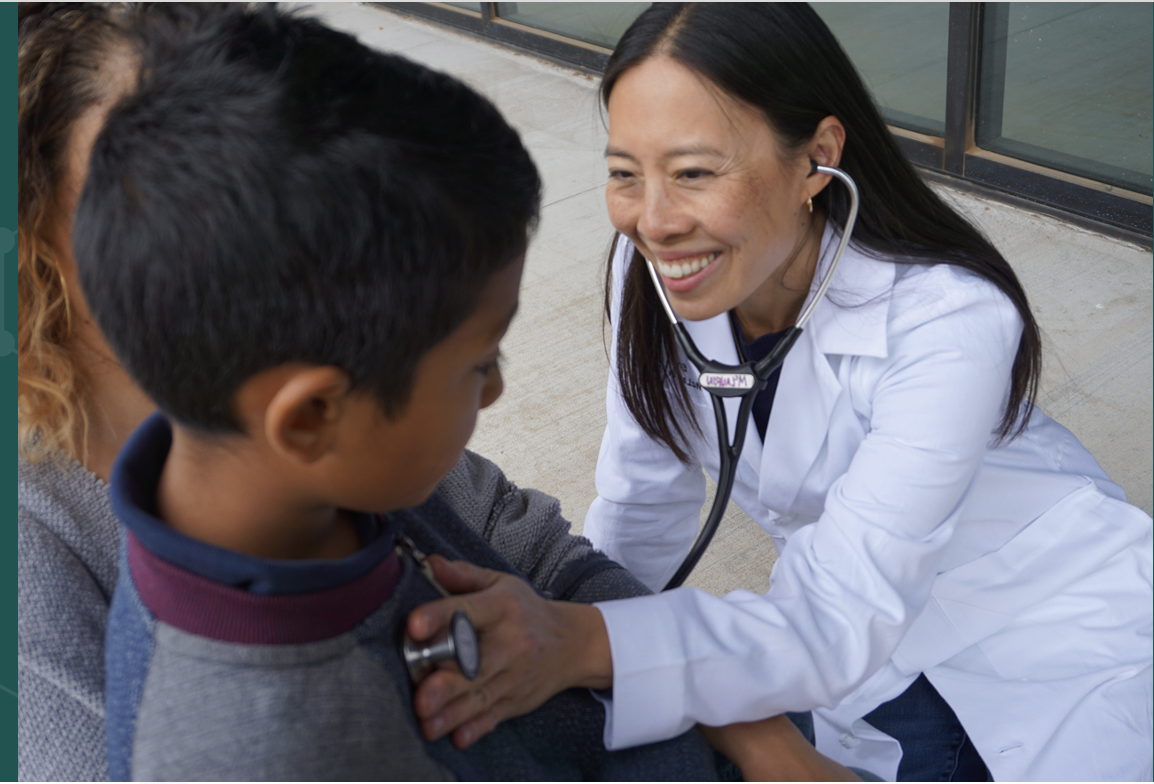 Dr. Emily McLaurin listening to a young patient with a stethoscope